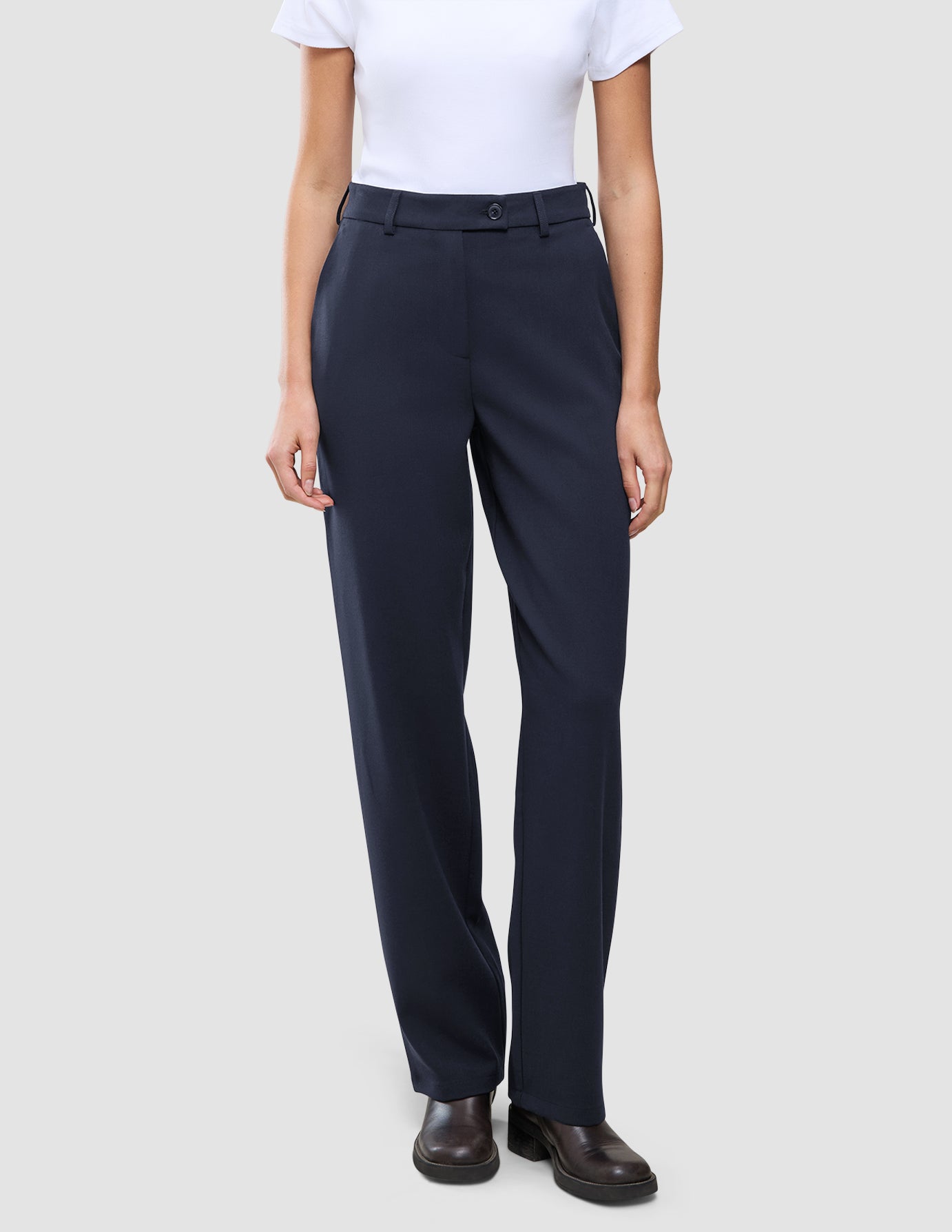 En person klädd i en vit t-shirt, Women GO2 Pants Straight Blue Nights och mörka skor, vilket återspeglar en skandinavisk estetik.