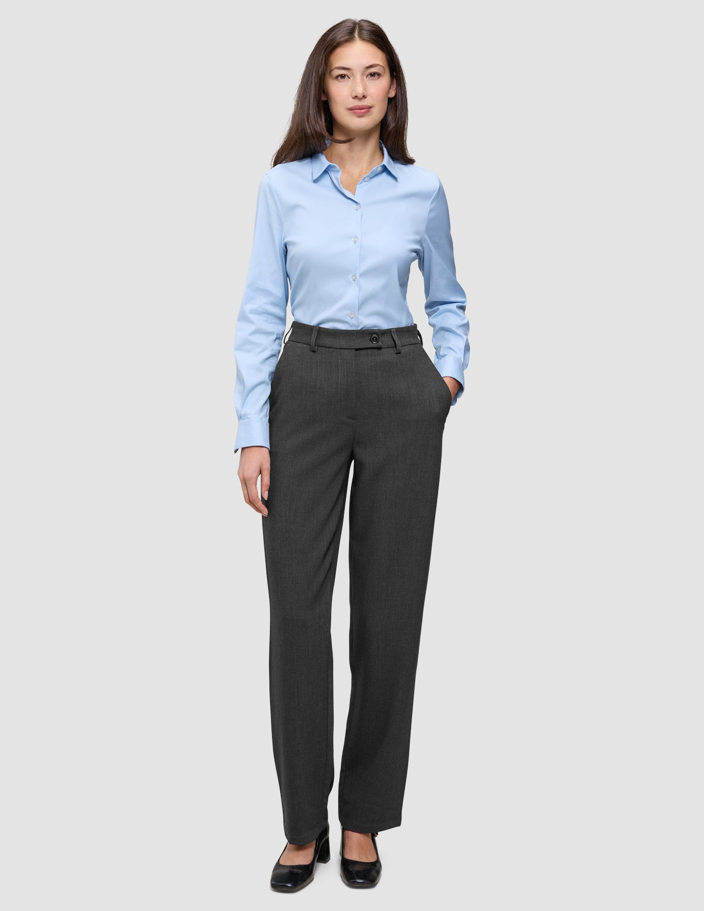 En kvinna klädd i en ljusblå skjorta med knappar och byxor av modellen Women GO2 Pants Straight i mörkgrå melange.
