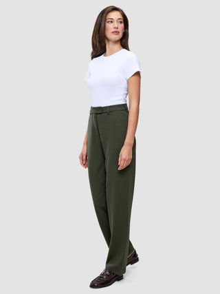 En kvinna bär en vit t-shirt instoppad i ett par högmidjade Women GO2 Pants Straight i färgen Dusty Olive samt mörka loafers.
