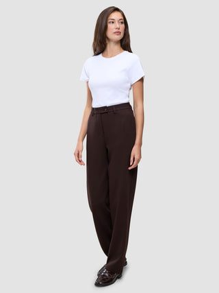 En kvinna bär en vit t-shirt och byxor av modellen Women GO2 Pants Straight Mocha i en rak, brun modell, tillsammans med mörka loafers.