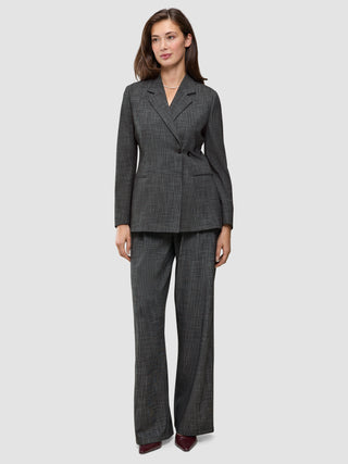 En kvinna bär en Women Nara Blazer Fitted Black Check i mörkgrå rutmönster tillsammans med matchande byxor med vida ben och 360°-stretch.