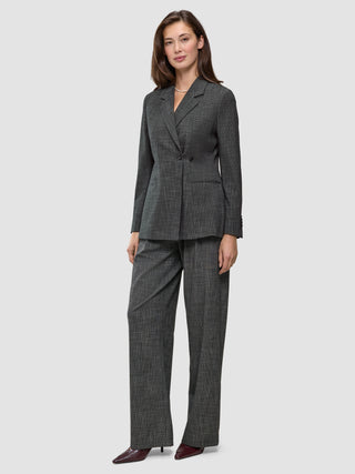 En kvinna bär en Nara-blazer för damer i svart rutmönster med figursydd passform och matchande kolgrå rutiga byxor med vid benöppning och 360°-stretch.
