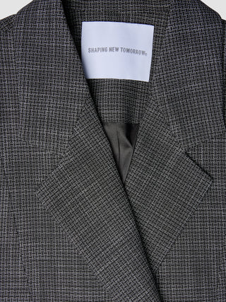 Närbild på en svartvit rutig damblazer av modellen Nara Blazer Fitted Black Check med en etikett i nacken med texten SHAPING NEW TOMORROW.