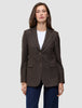 En kvinna bär en brun, valnötsfärgad Women Serene Blazer Regular i fiskbensmönster över en vit t-shirt och mörkblå jeans.