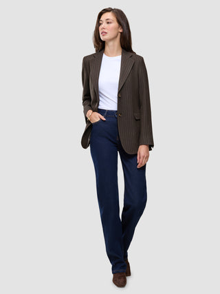 En kvinna klädd i en Women Serene Blazer Regular Walnut Herringbone över en vit t-shirt och mörkblå jeans.