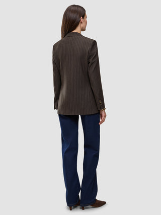 Bakifrånbild av en person klädd i en Women Serene Blazer Regular Walnut Herringbone, mörkblå jeans och bruna skor med ullfinish.