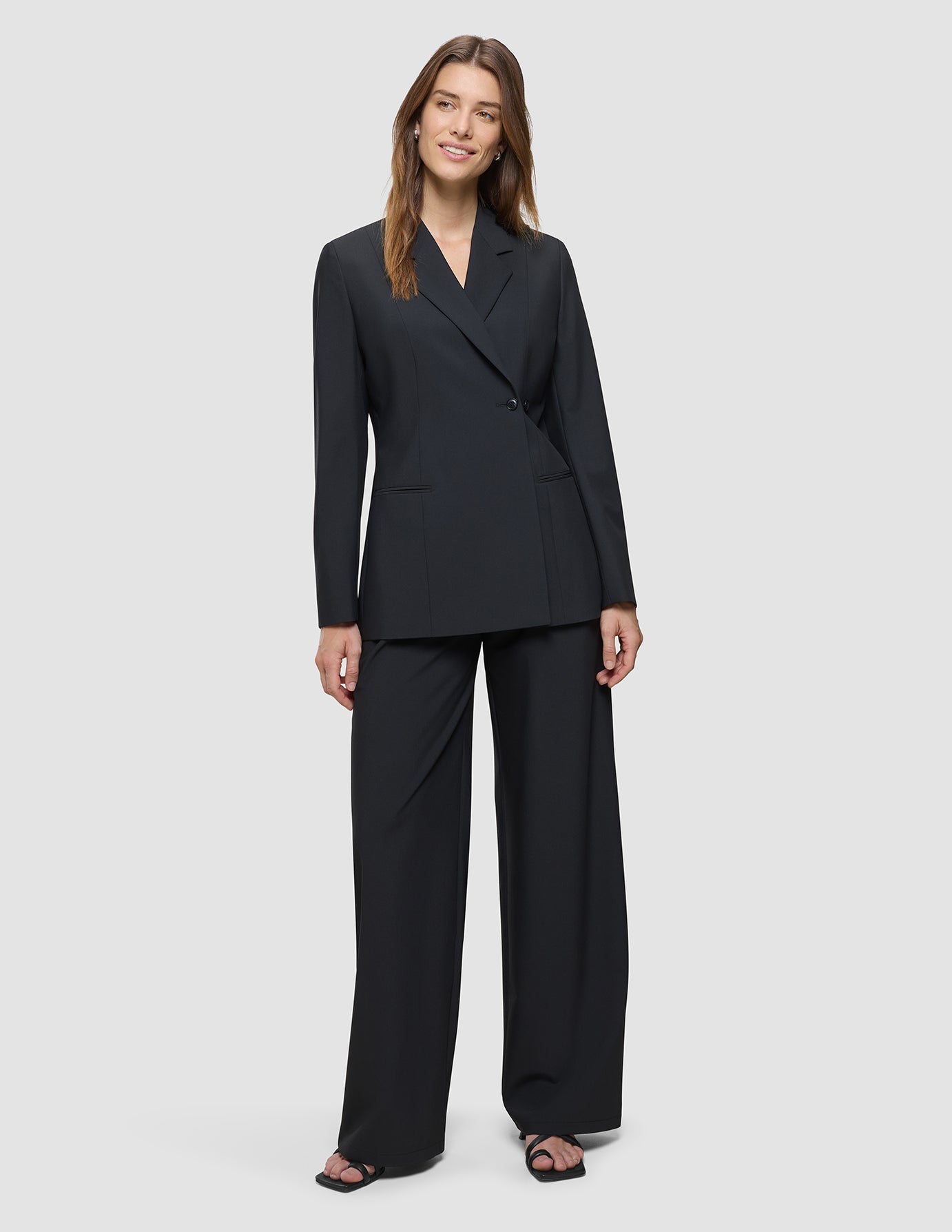 En kvinna klädd i en svart Avira-kavaj för dam och matchande byxor med vida ben för en festlig look.