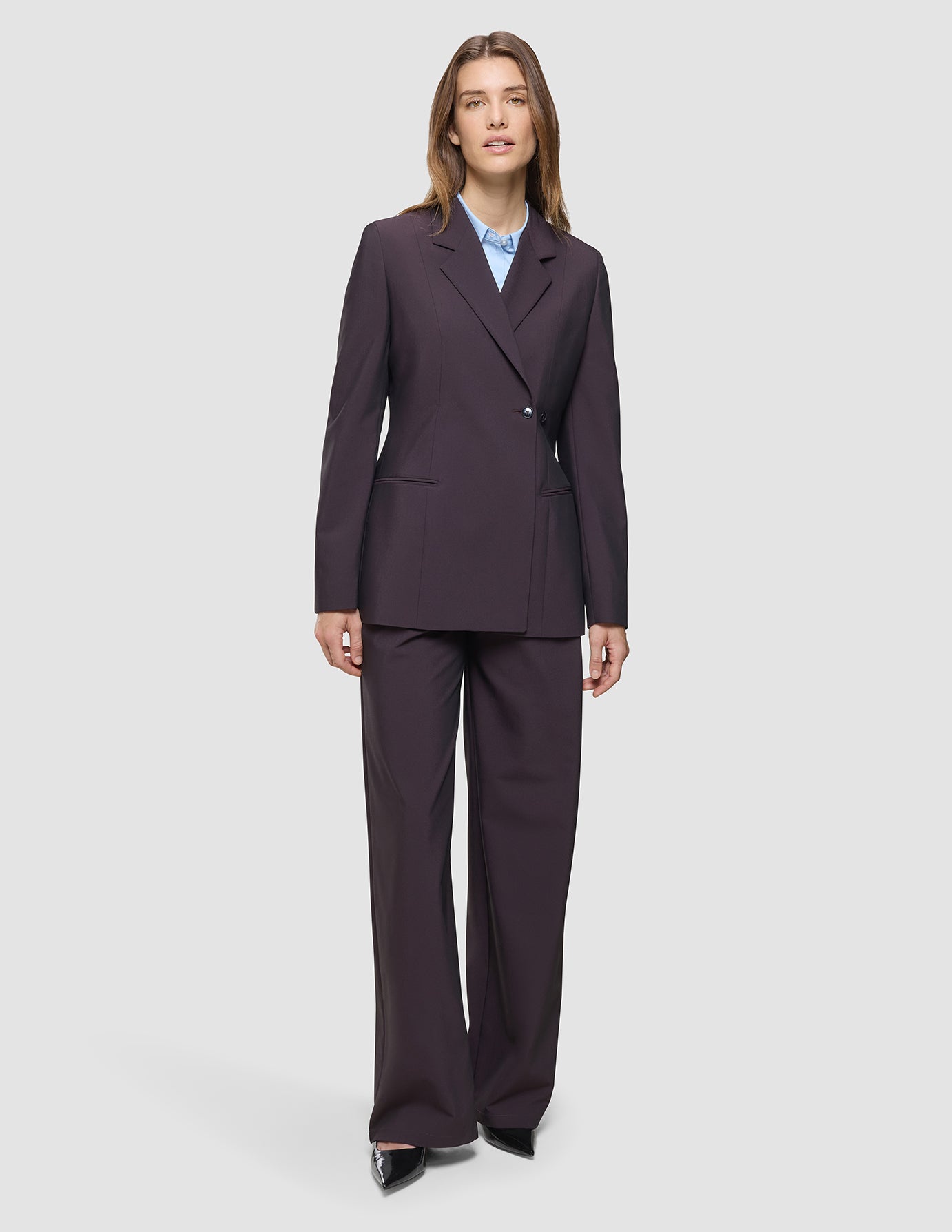 En kvinna klädd i en Avira-blazer för damer i färgen ”Burgundy Berry”, som hon bär över en ljusblå skjorta med krage.