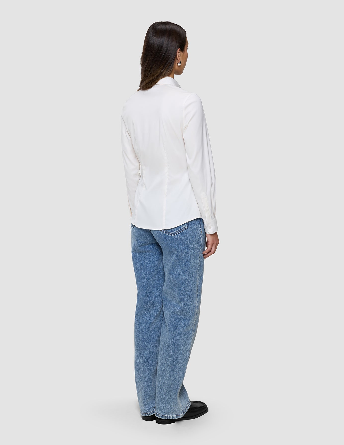 Bakifrånbild av en person som bär en vit Women’s Oxford Shirt White Orchid Slim instoppad i ljusblå jeans.