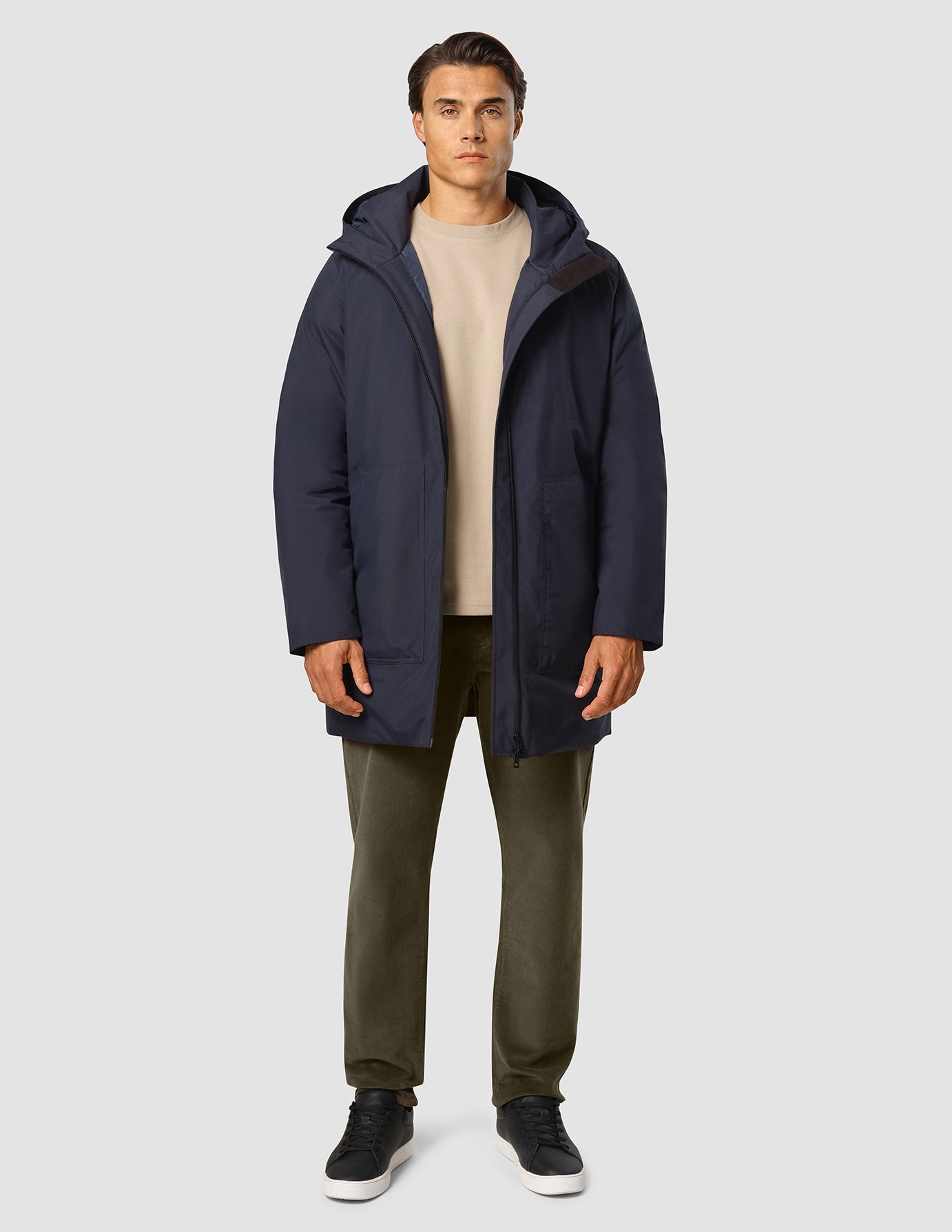 En man klädd i en mörkblå Utility Jacket över en beige tröja och mörk olivgröna byxor.
