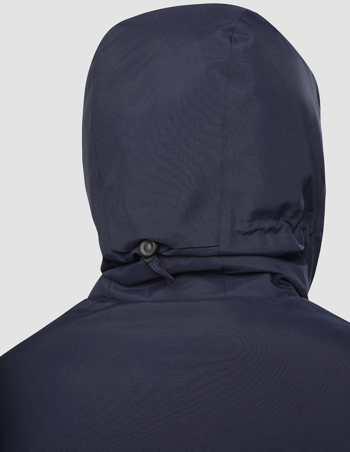 Baksidan av en Utility Jacket i mörk marinblått med en snörjustering längst ner på huvan.