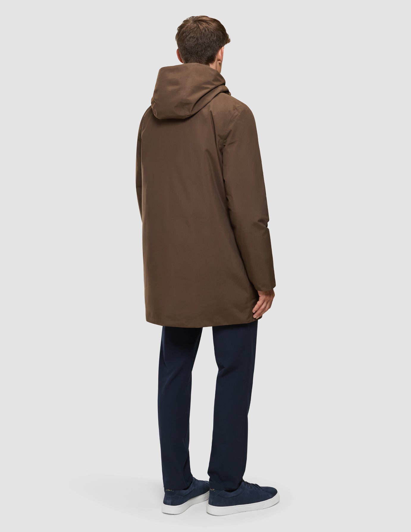 En man sedd bakifrån, klädd i en Utility Jacket i färgen Saddle Brown, mörka byxor och blå sneakers.