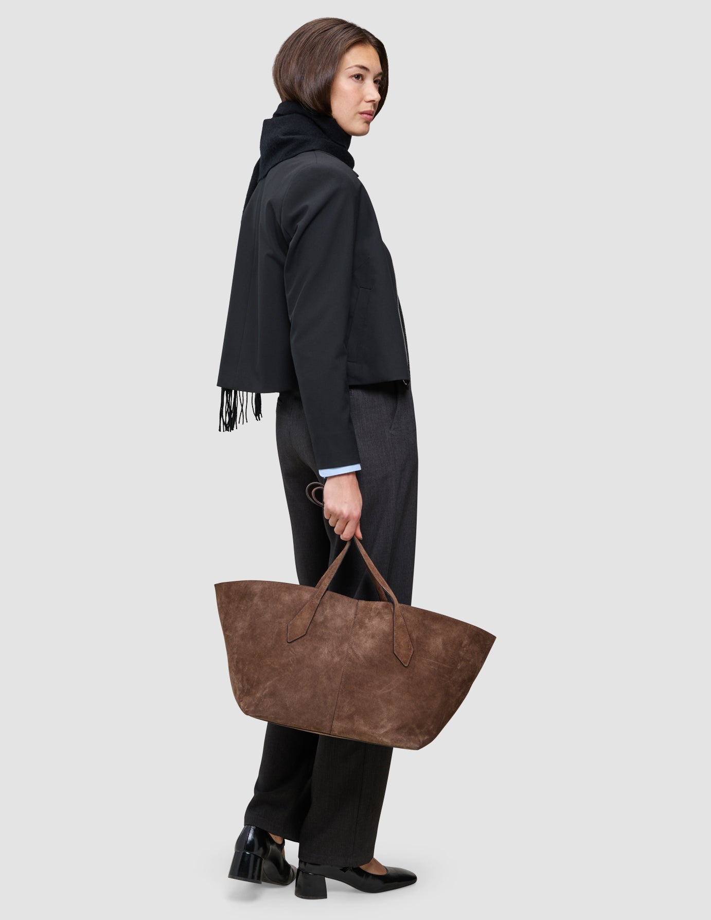 En person klädd i en Essential Zip Jacket och Go2 Pants från kollektionen An easy office upgrade håller i en stor brun väska i mocka.