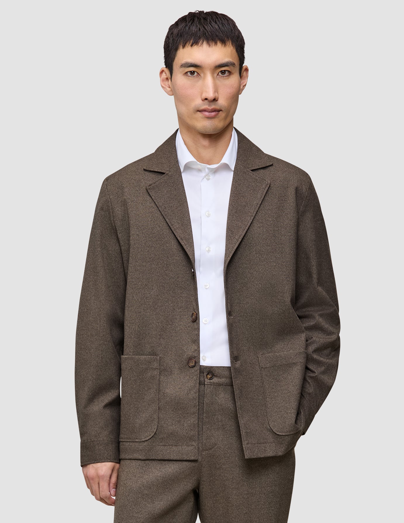 En man bär en brun, rutig Atelier Overshirt Dark Beige över en vit skjorta med knappar.
