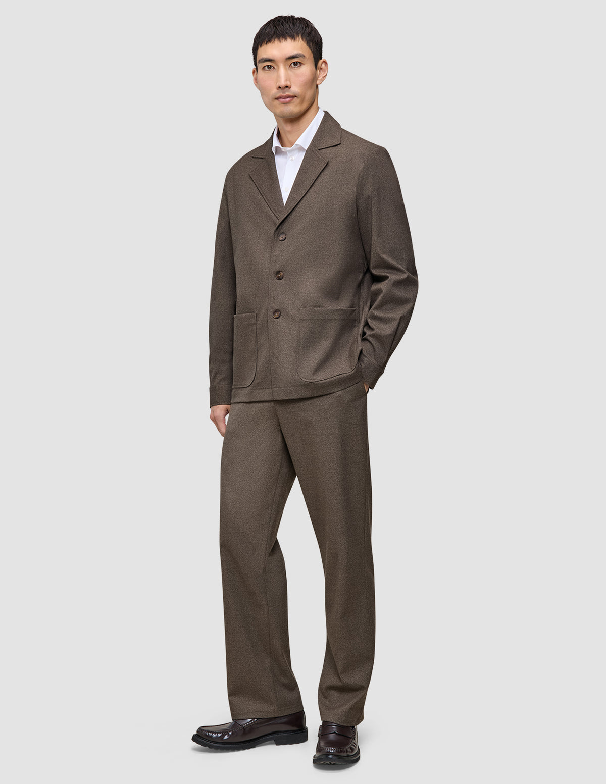 En man klädd i en mörkbeige overshirt från Atelier, vit skjorta och matchande byxor samt mörka loafers.