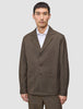 En man klädd i en mörkbeige Atelier Overshirt i brutet twill över en vit skjorta med krage.