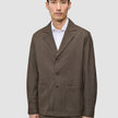 En man klädd i en mörkbeige Atelier Overshirt i brutet twill över en vit skjorta med krage.