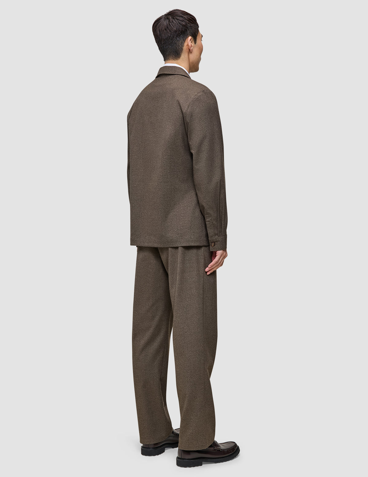 En man sedd bakifrån, klädd i en brun Atelier Overshirt Dark Beige och matchande byxor samt mörka loafers.