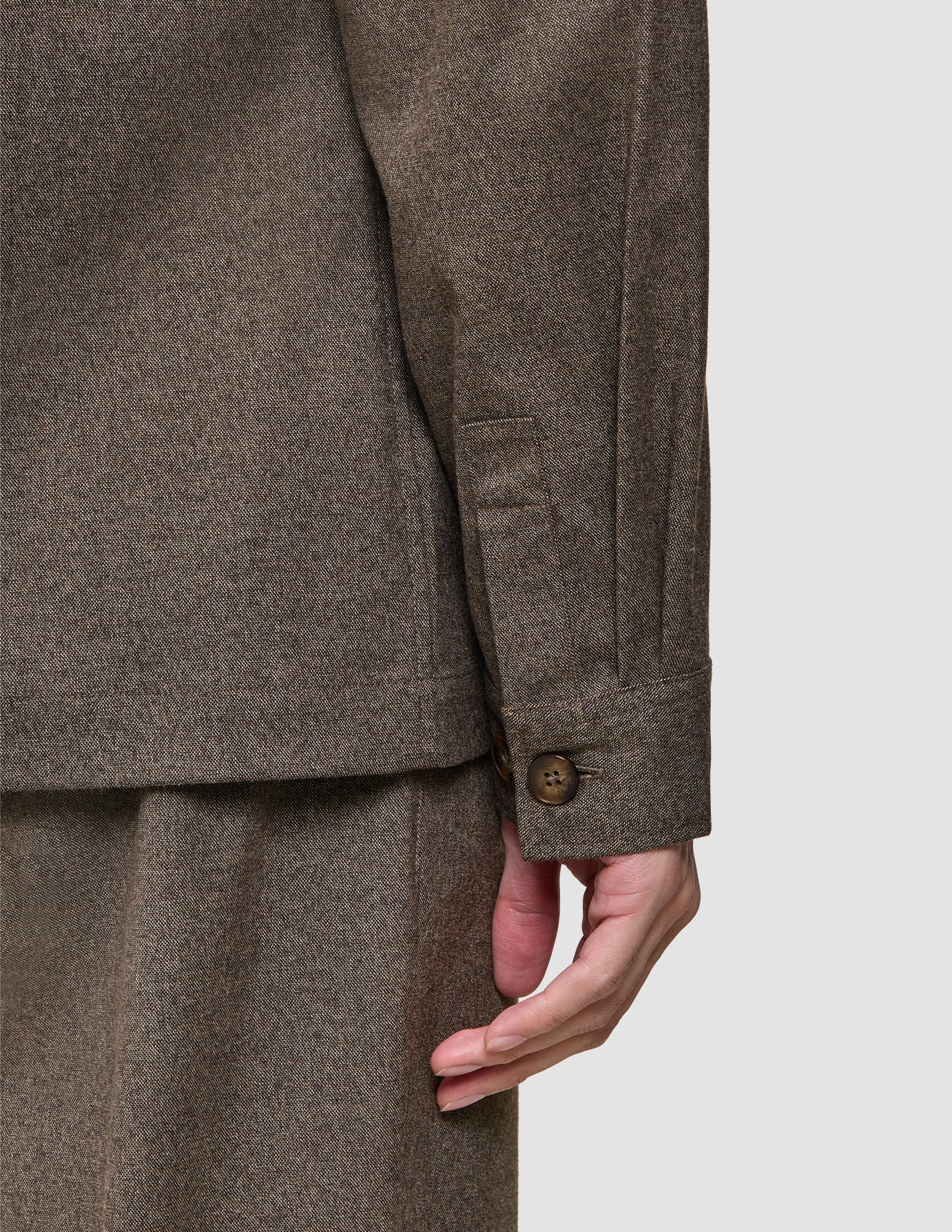 Närbild på en långärmad övertröja från Atelier i mörkbeige, med manschetter i bruten twill och en enda knapp.