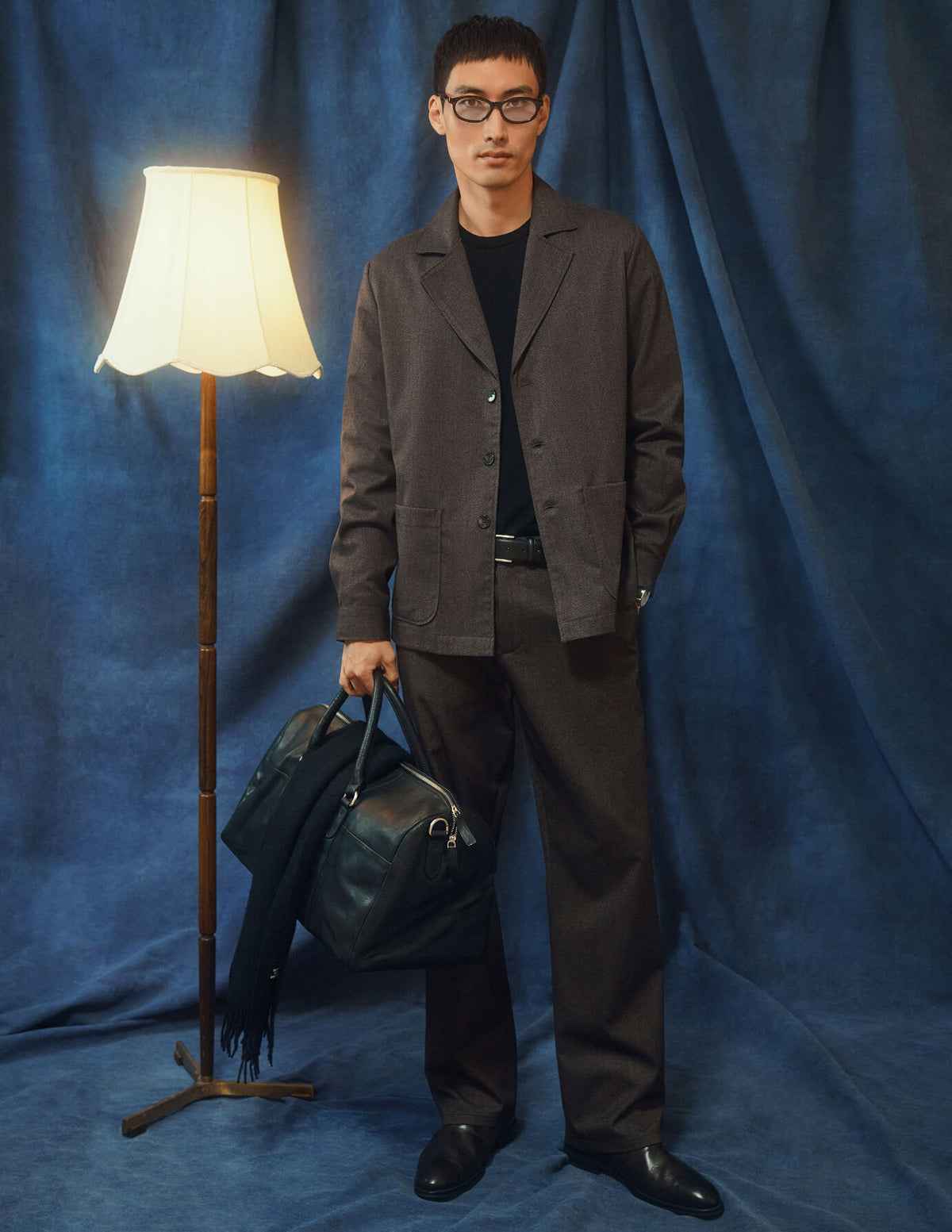 En man klädd i en mörkbeige overshirt från Atelier och matchande byxor, som håller i en svart läderduffelväska.