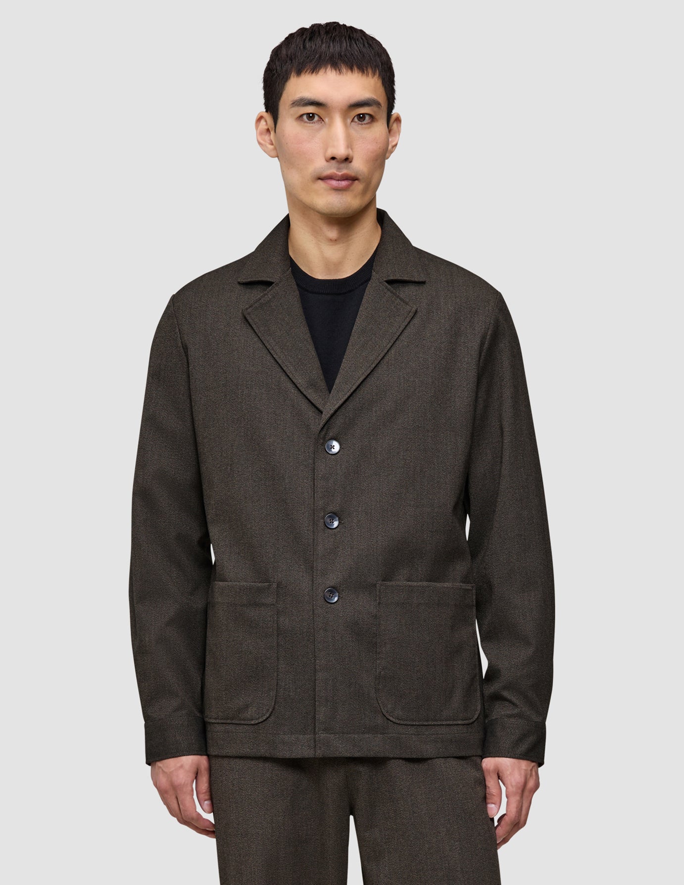 En man klädd i en Atelier Overshirt i mörkbrun bruten twill med en krage med skåra och två påsydda fickor framtill.