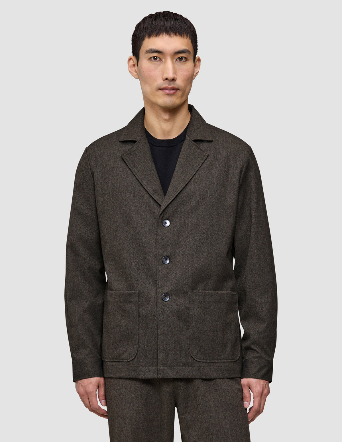 En man klädd i en Atelier Overshirt i mörkbrun bruten twill med en krage med skåra och två påsydda fickor framtill.