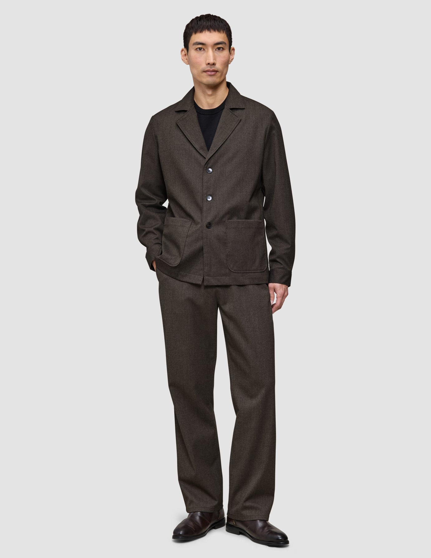 En man klädd i en Atelier Overshirt i mörkbrun bruten twill och matchande byxor.
