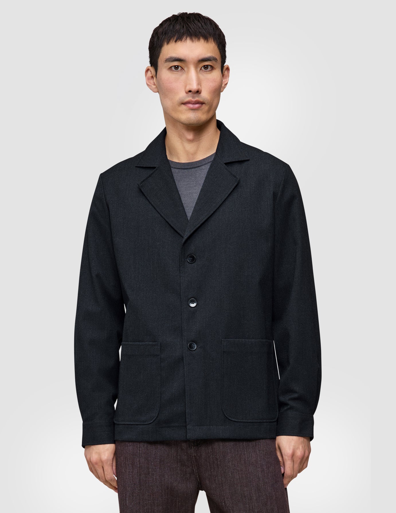 En person bär en mörkblå Atelier-överskjorta i bruten twill med krage och två framfickor.
