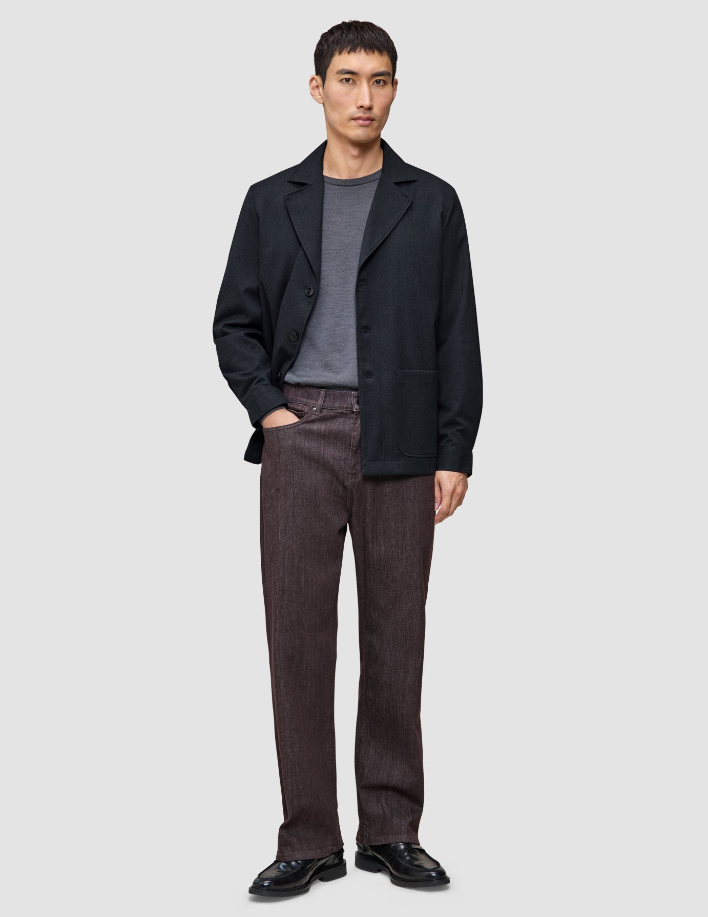 En man klädd i en mörkblå Atelier Overshirt över en grå t-shirt, bruna byxor och svarta loafers.