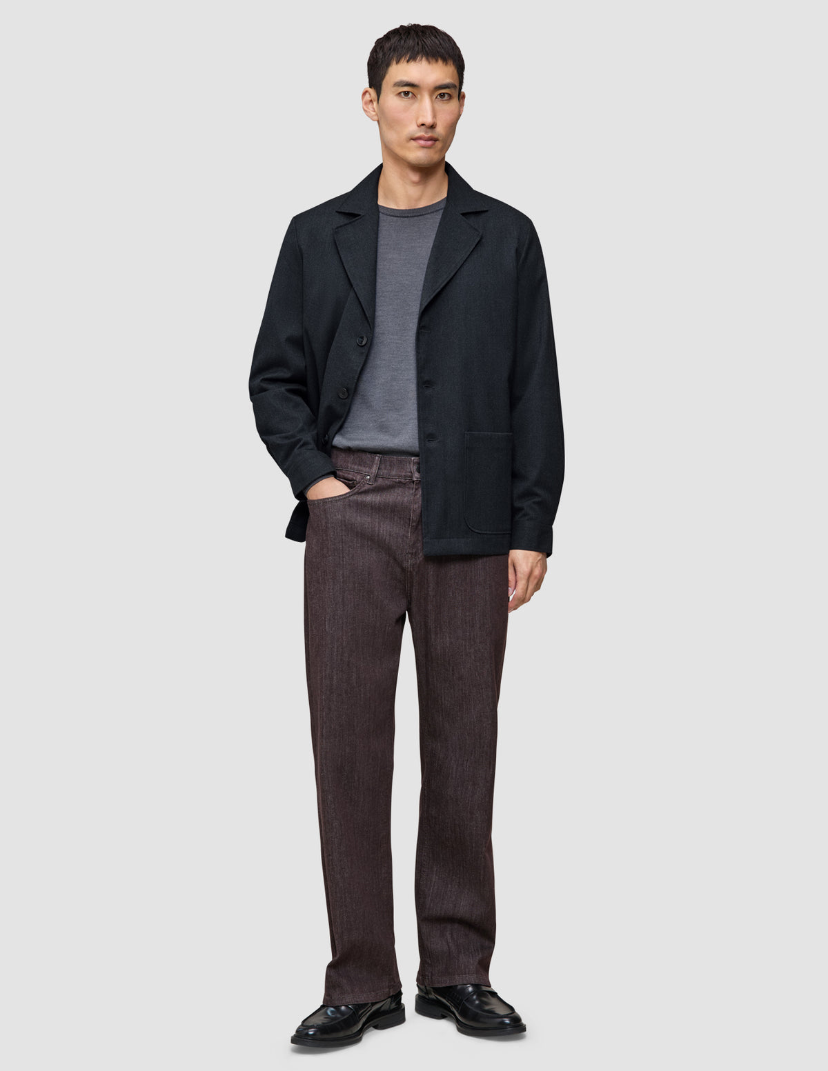 En man klädd i en mörkblå Atelier Overshirt över en grå t-shirt, bruna byxor och svarta loafers.