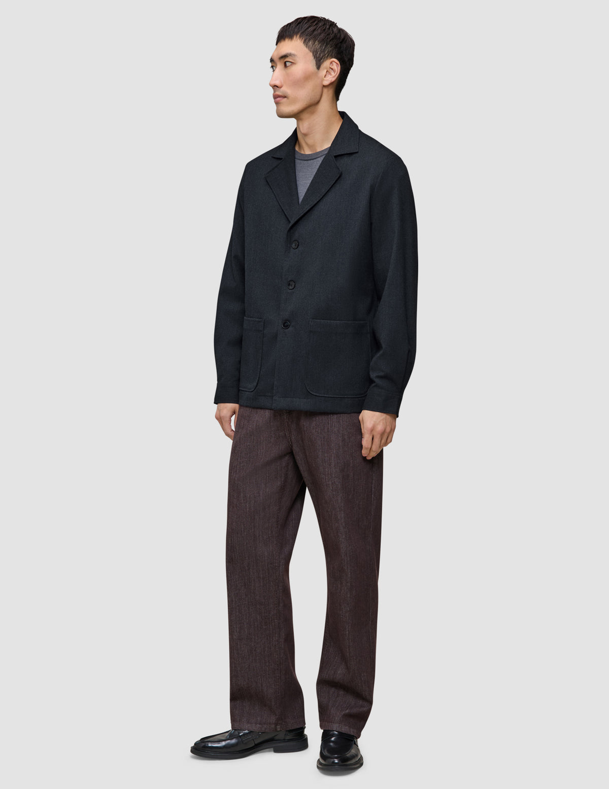 En man klädd i en mörkblå Atelier Overshirt, en grå t-shirt och mörka byxor.