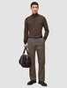 En man klädd i en brun tröja med kvartslång dragkedja och byxor av modellen Atelier Pants Relaxed Dark Beige, som håller i en mörk väska.