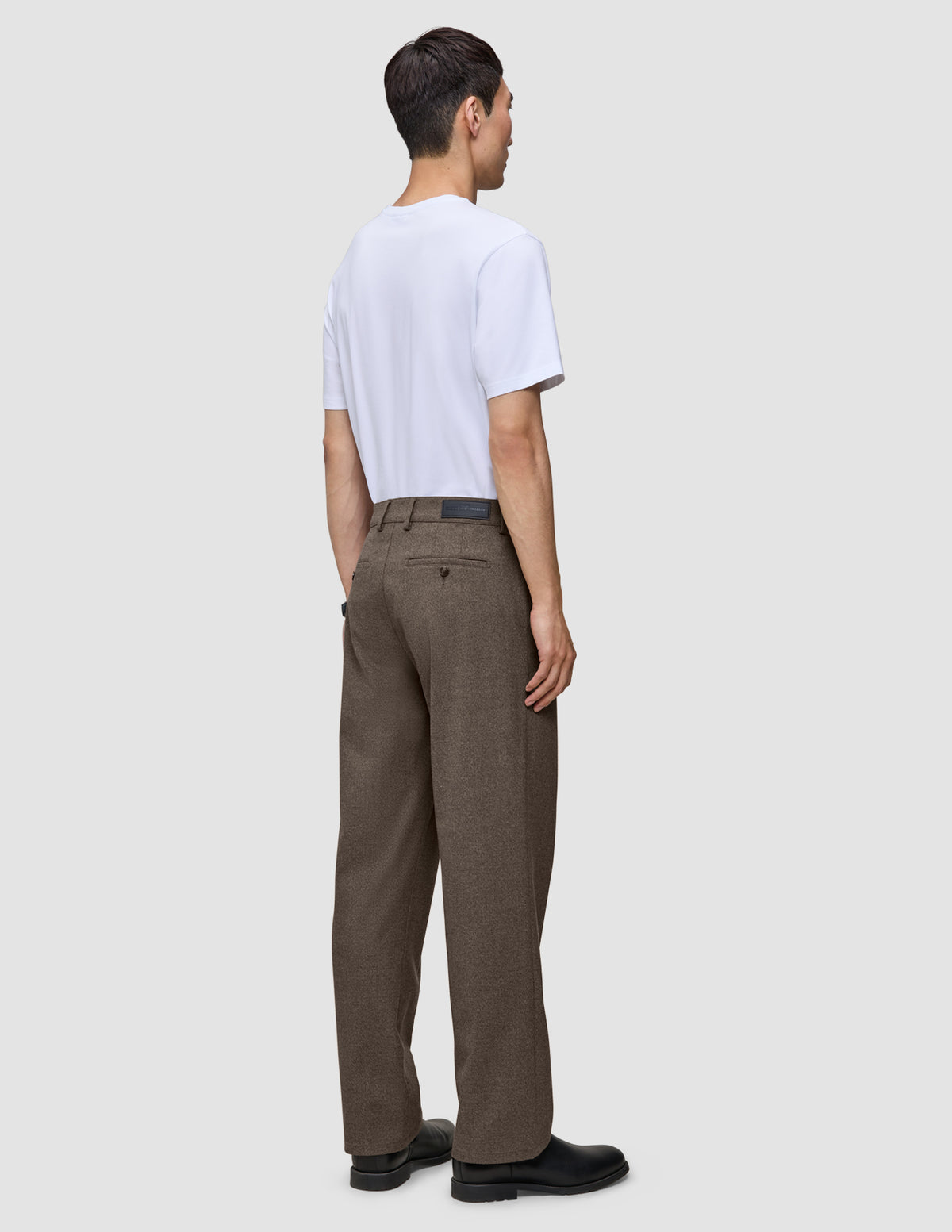En man sedd bakifrån, klädd i en vit t-shirt och ett par löst sittande byxor i skandinavisk design, Atelier Pants Relaxed Dark Beige.