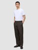En person i en vit t-shirt och mörkbruna Atelier Pants Relaxed med avslappnad passform, med händerna i fickorna.