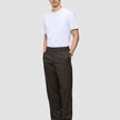 En person i en vit t-shirt och mörkbruna Atelier Pants Relaxed med avslappnad passform, med händerna i fickorna.