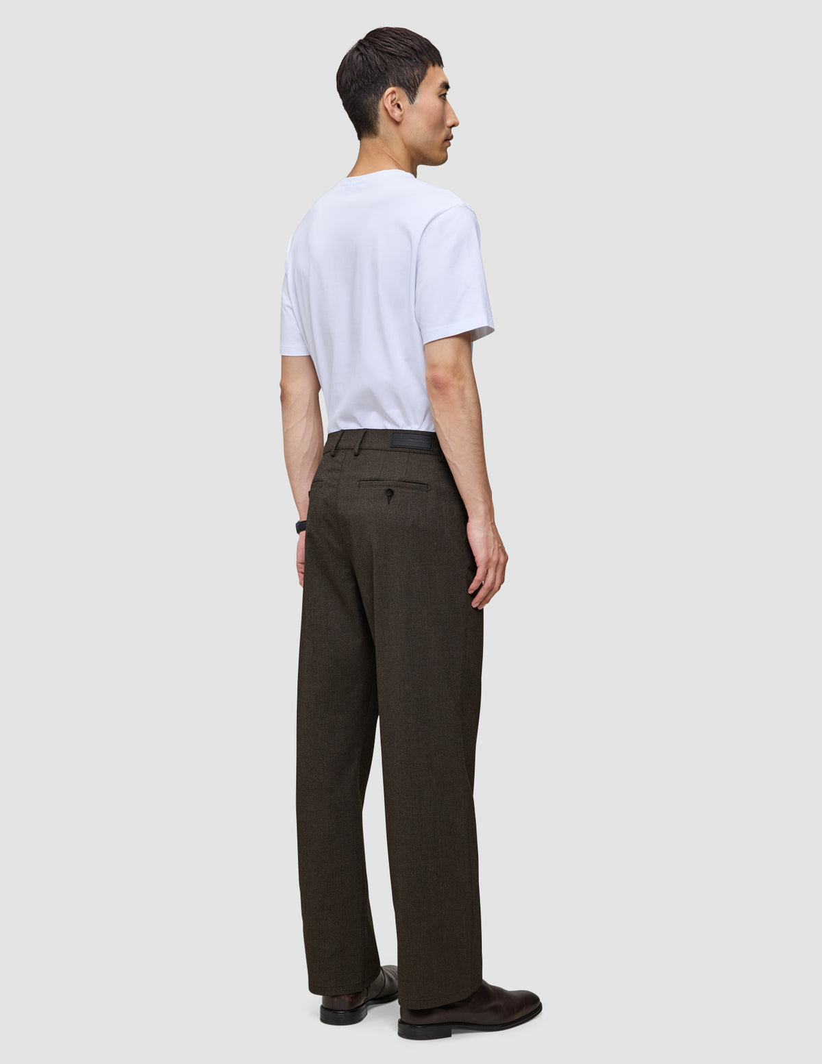 En man sedd bakifrån, klädd i en vit t-shirt och mörkbruna Atelier Pants Relaxed.