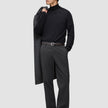 En man i svart polotröja och ett par Atelier Pants Relaxed i mörkgrått med avslappnad passform, med en kappa över axeln.
