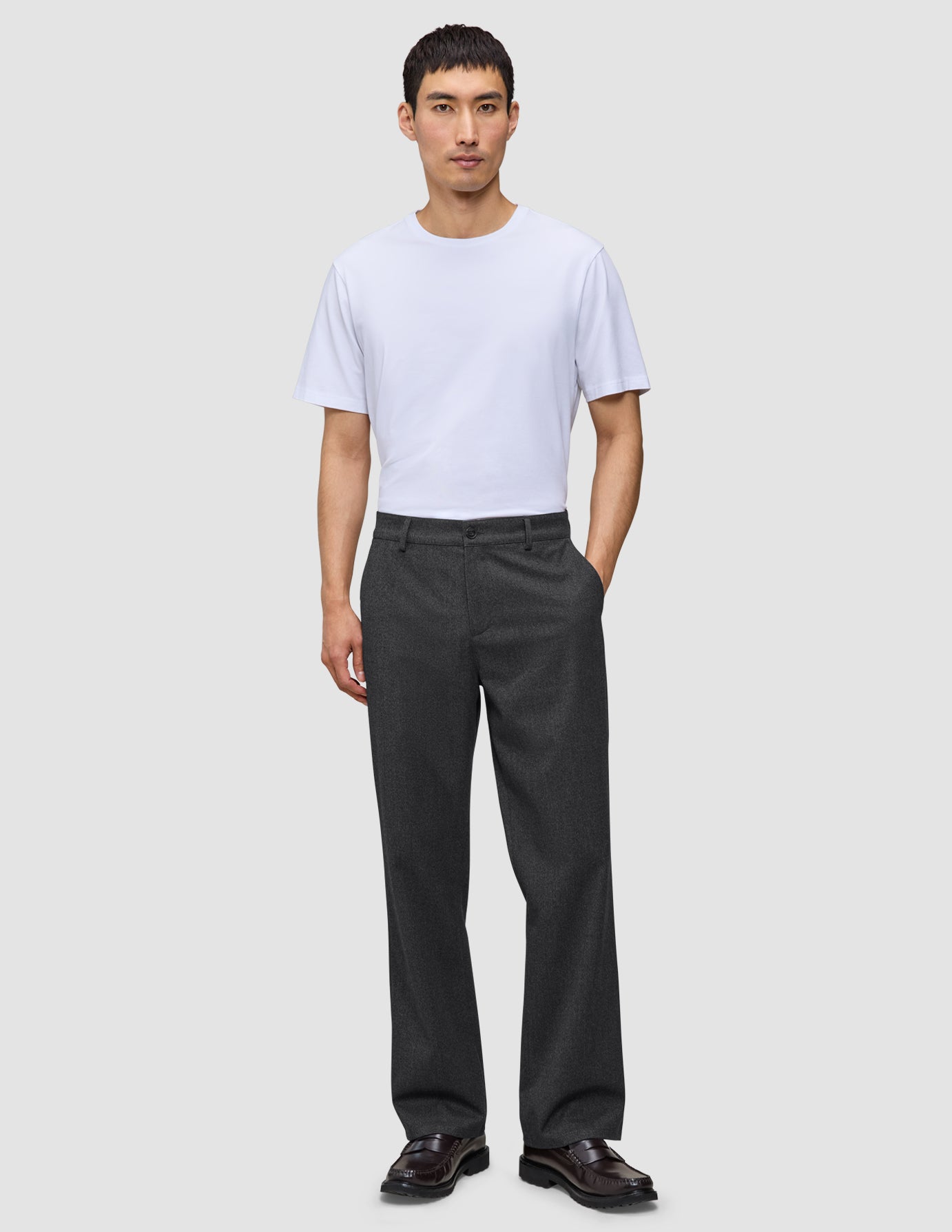 En man klädd i en vit t-shirt och byxor av modellen Atelier Pants Relaxed Dark Grey i bruten twill.