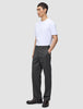 En person bär en vit t-shirt, byxor av modellen Atelier Pants Relaxed i mörkgrått och mörka loafers.