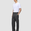 En person bär en vit t-shirt, byxor av modellen Atelier Pants Relaxed i mörkgrått och mörka loafers.
