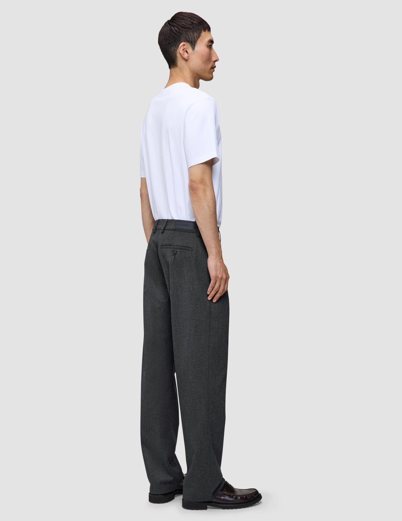 En person i profil bär en vit t-shirt och ett par Atelier Pants Relaxed i mörkgrått med avslappnad passform.