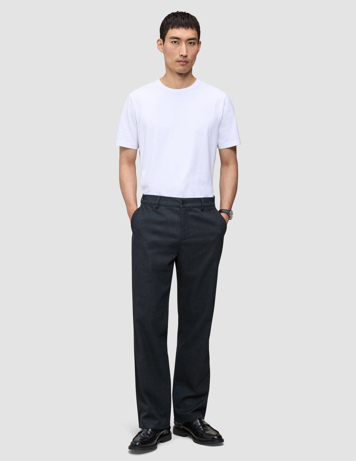 En man bär en vit T-shirt med rund hals och byxor av modellen Atelier Pants Relaxed Dark Navy i bruten twill.