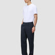 En man klädd i en vit t-shirt och byxor av modellen Atelier Pants Relaxed Dark Navy i bruten twill.