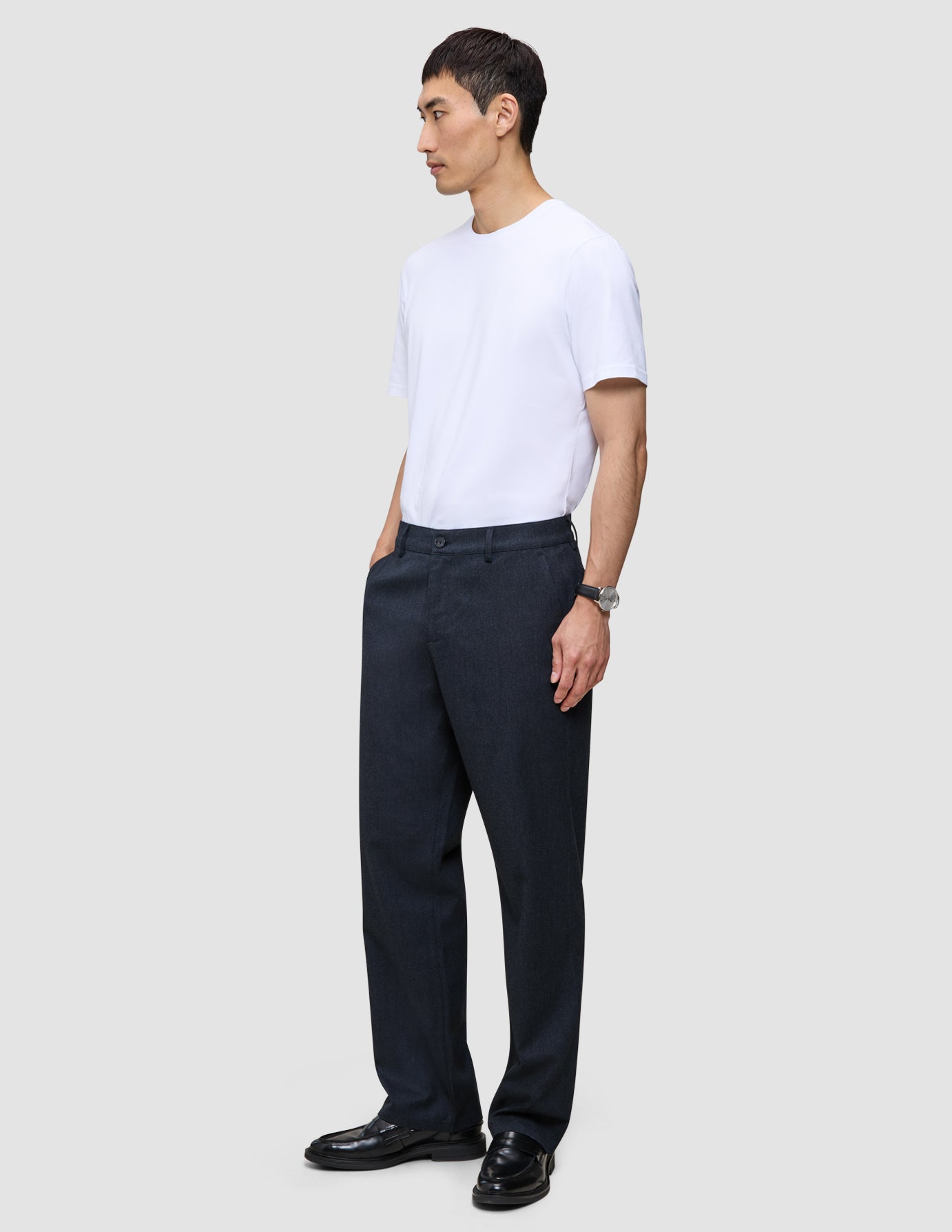 En man klädd i en vit t-shirt och byxor av modellen Atelier Pants Relaxed Dark Navy i bruten twill.