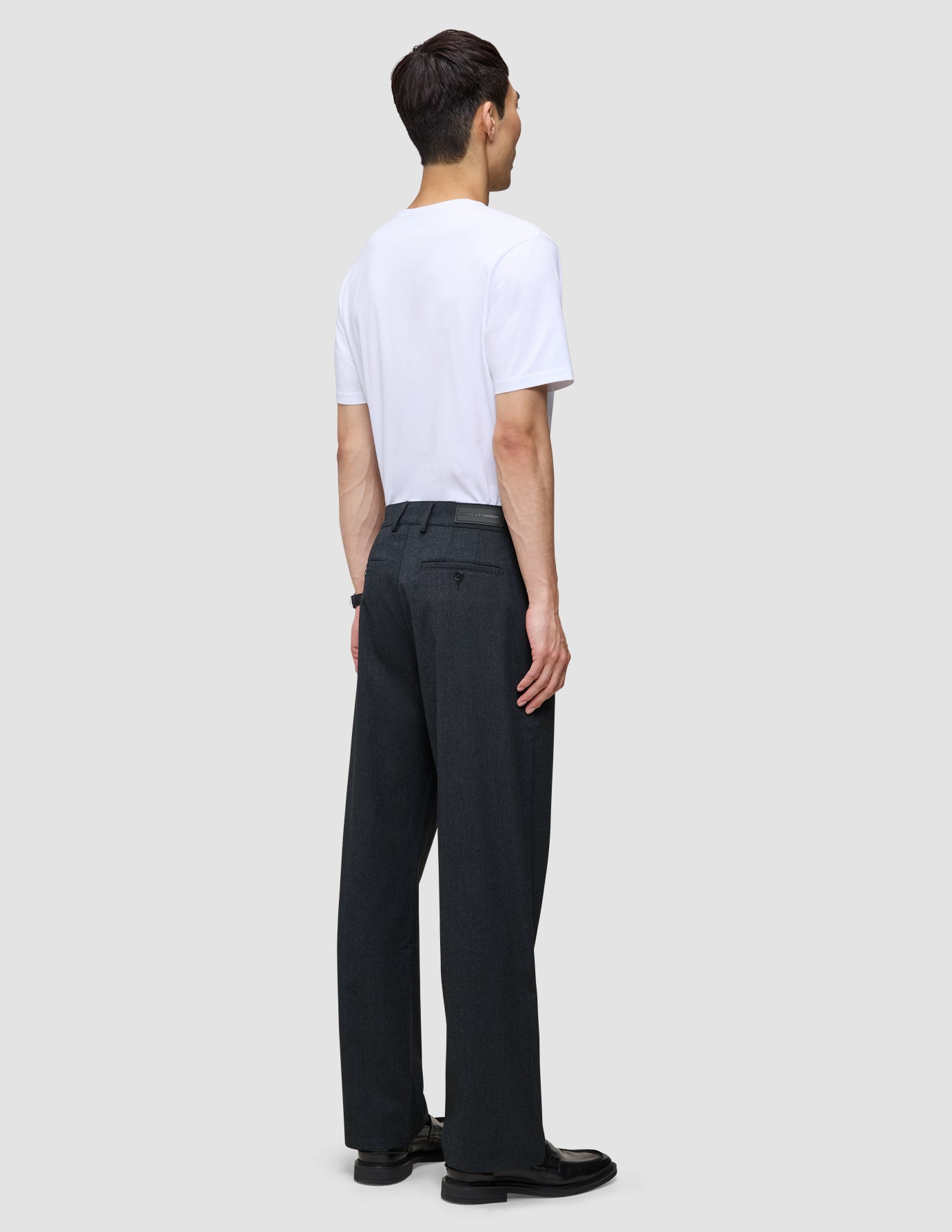 En person sedd bakifrån, klädd i en vit t-shirt och byxor av modellen Atelier Pants Relaxed Dark Navy.
