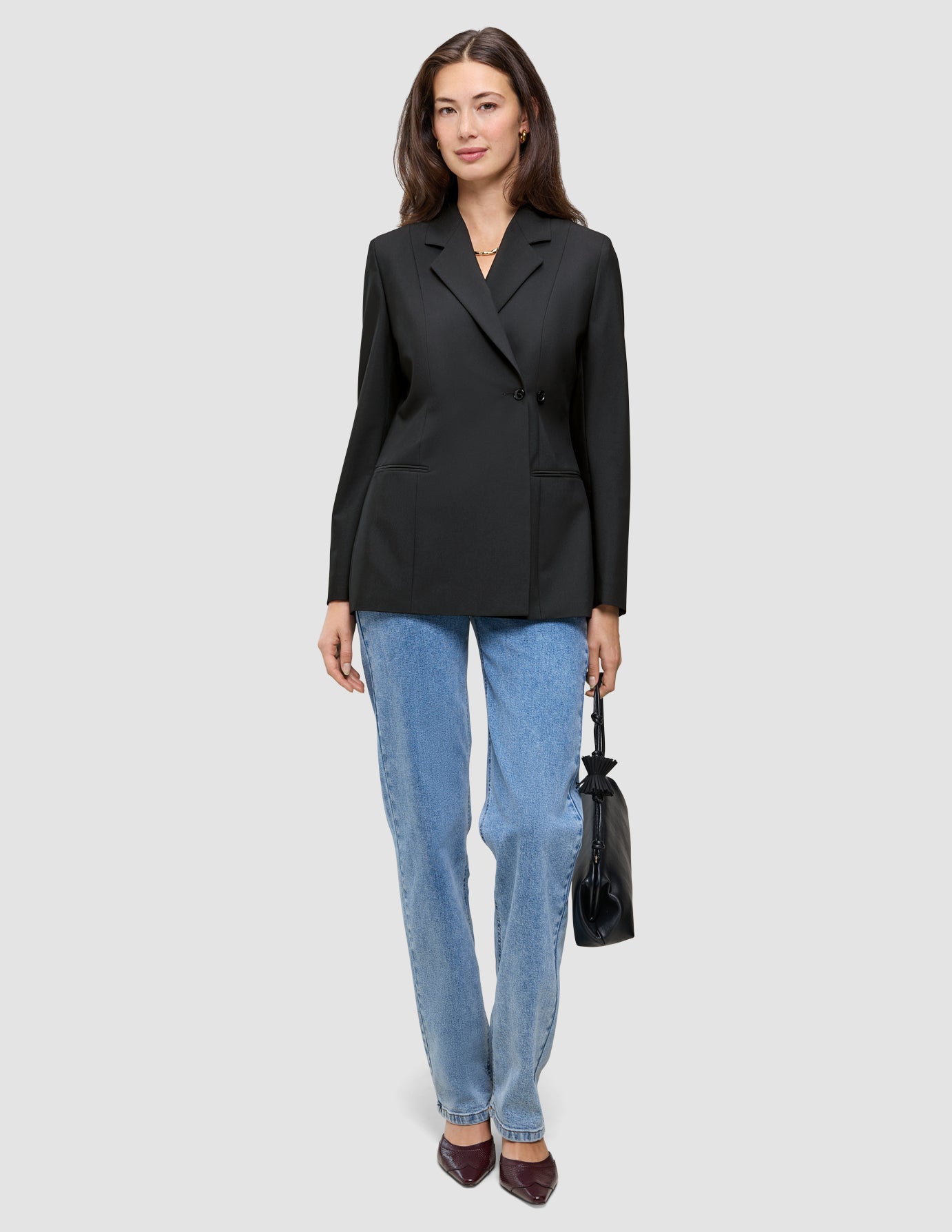 En kvinna klädd i en svart Avira-kavaj för damer och blå jeans, som håller i en liten svart handväska.