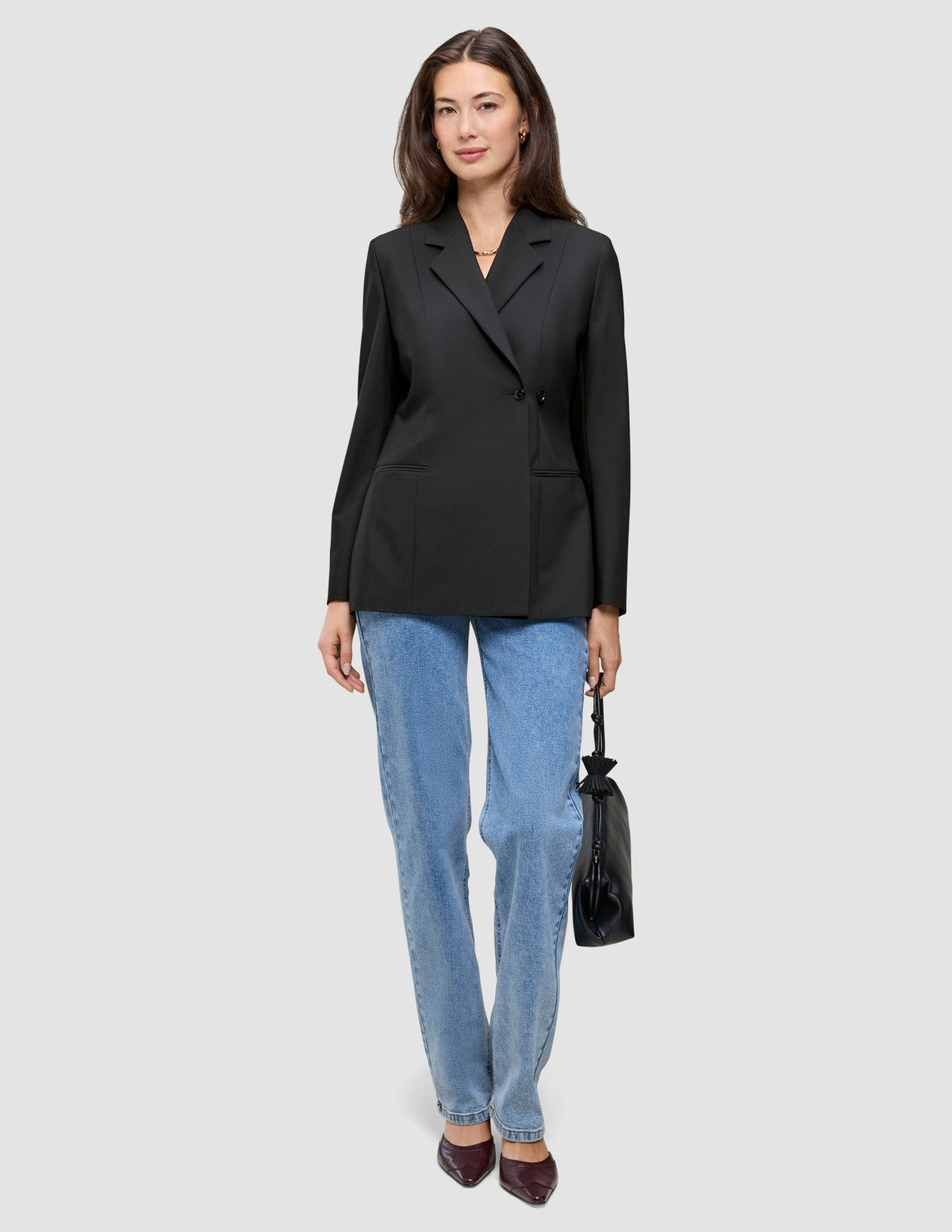 En kvinna klädd i en svart Avira-kavaj för damer och blå jeans, som håller i en liten svart handväska.