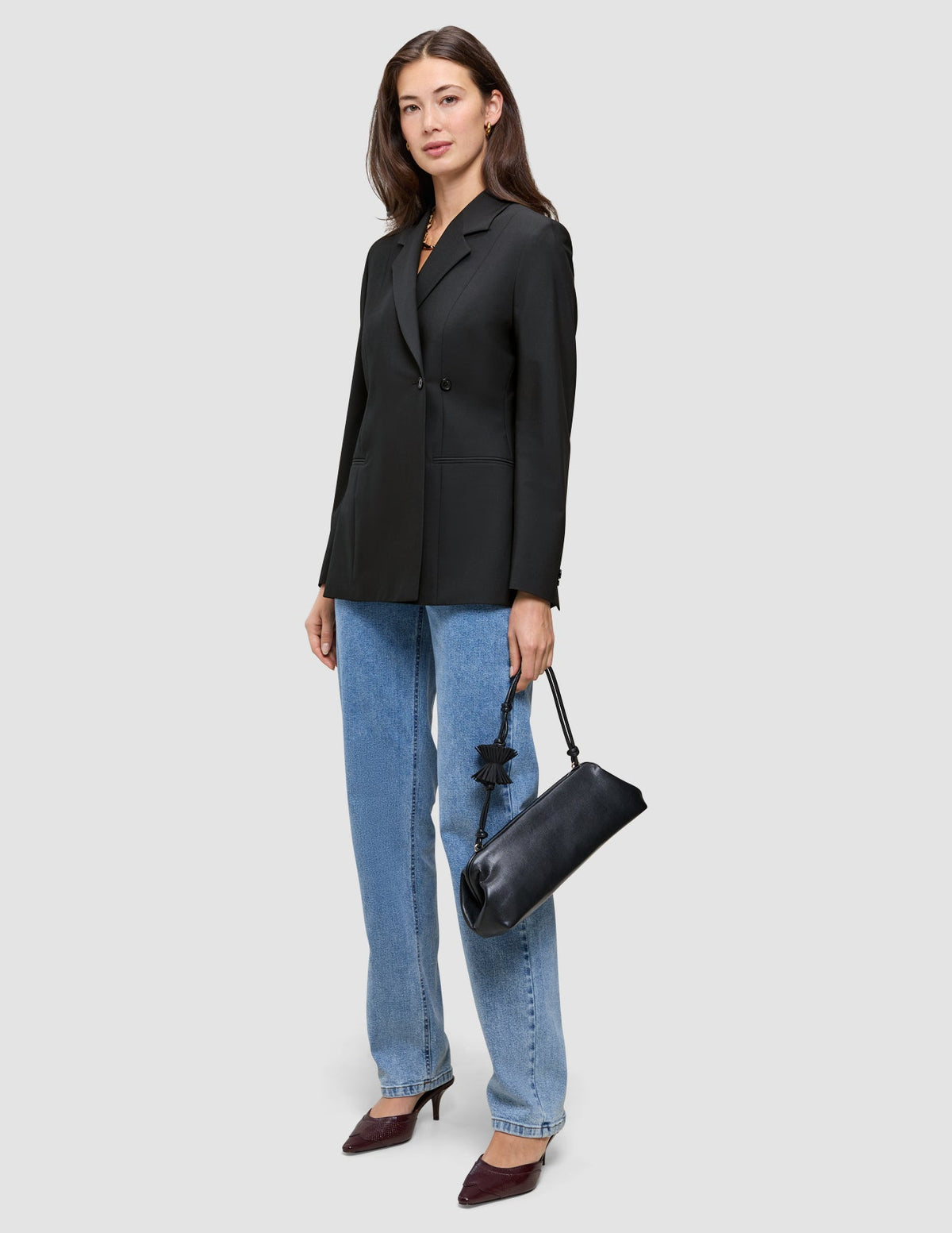 En kvinna klädd i en svart Avira-kavaj för damer i dubbelknäppt modell, tillsammans med blå jeans och en svart axelväska.
