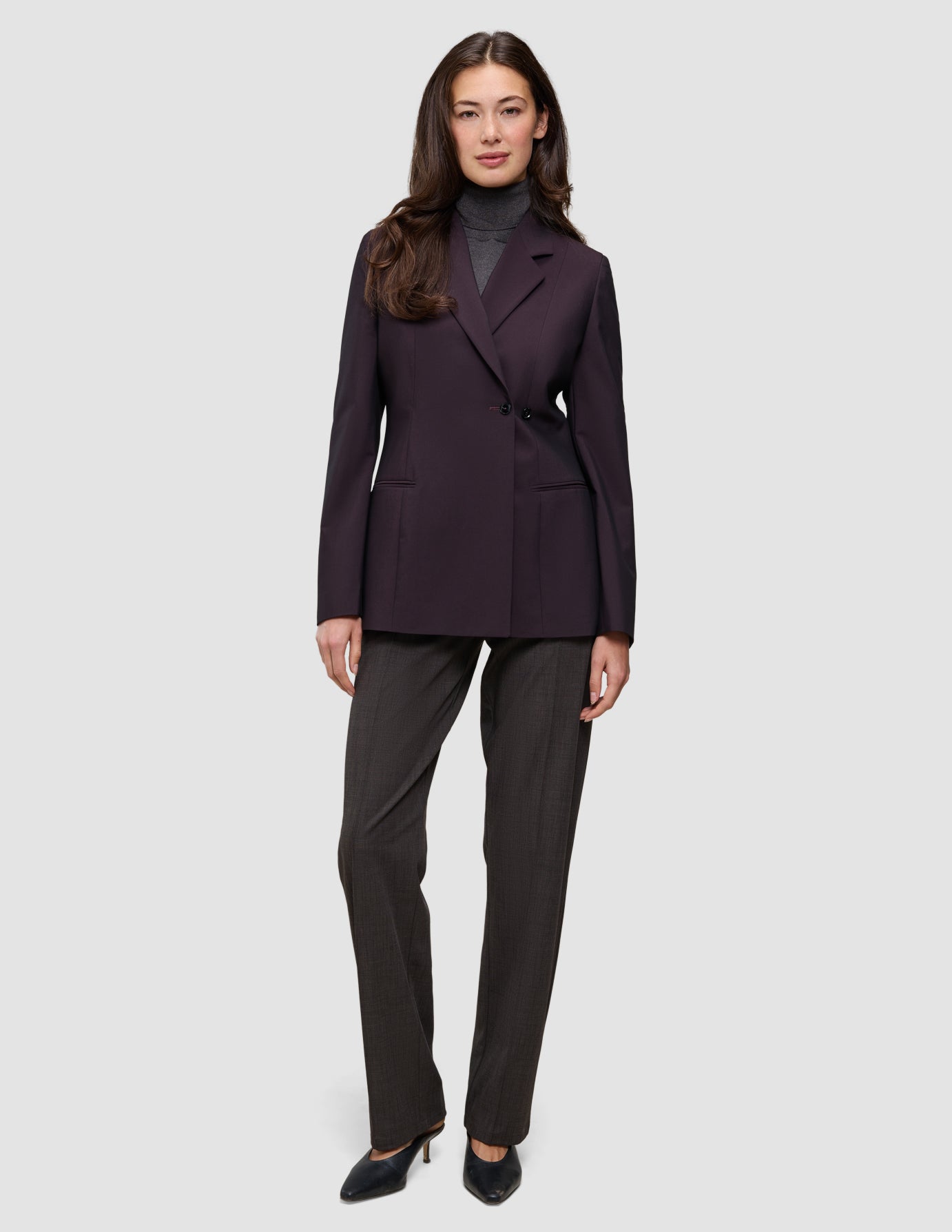En kvinna klädd i en mörklila Women’s Avira Blazer Burgundy Berry över en grå polotröja och mörka byxor.