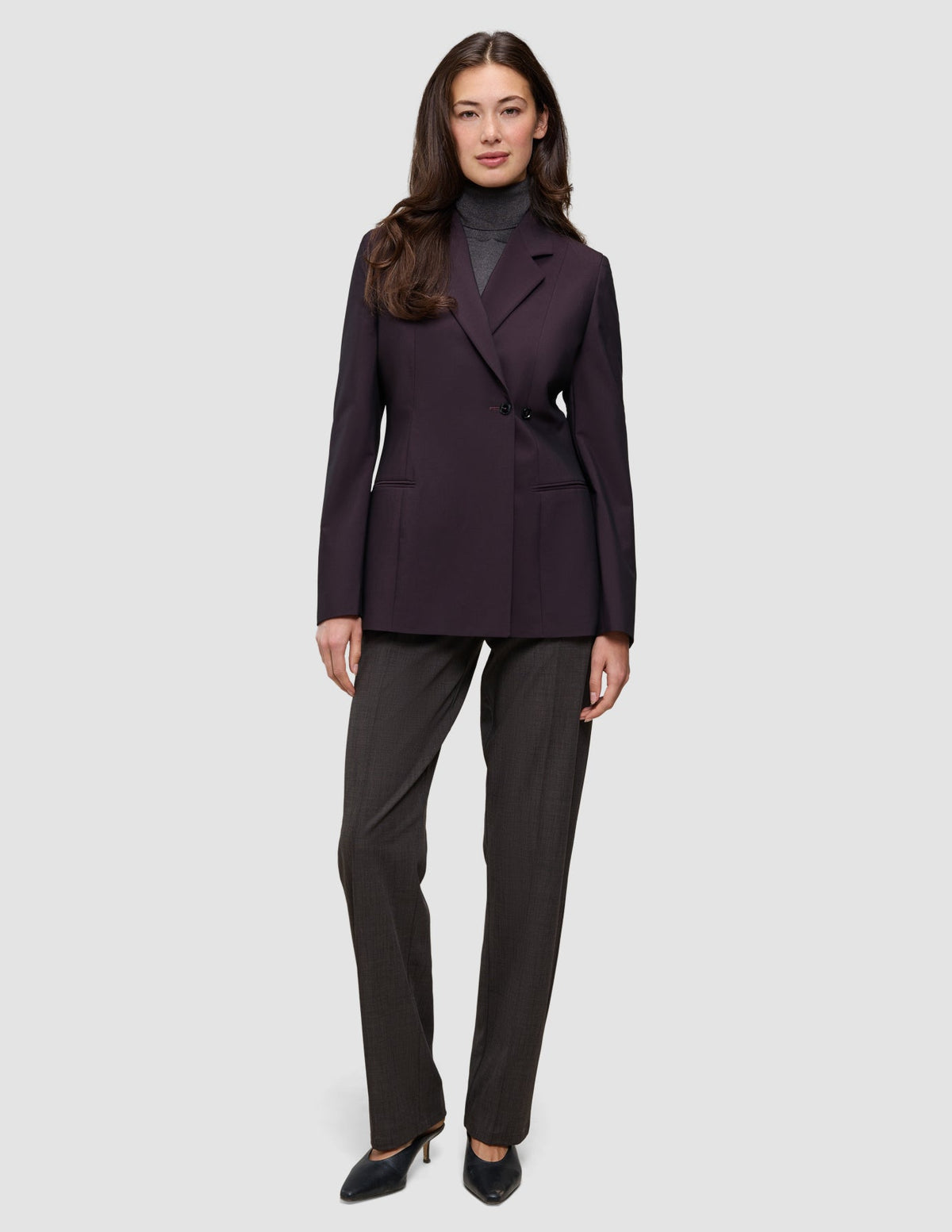 En kvinna klädd i en mörklila Women’s Avira Blazer Burgundy Berry över en grå polotröja och mörka byxor.